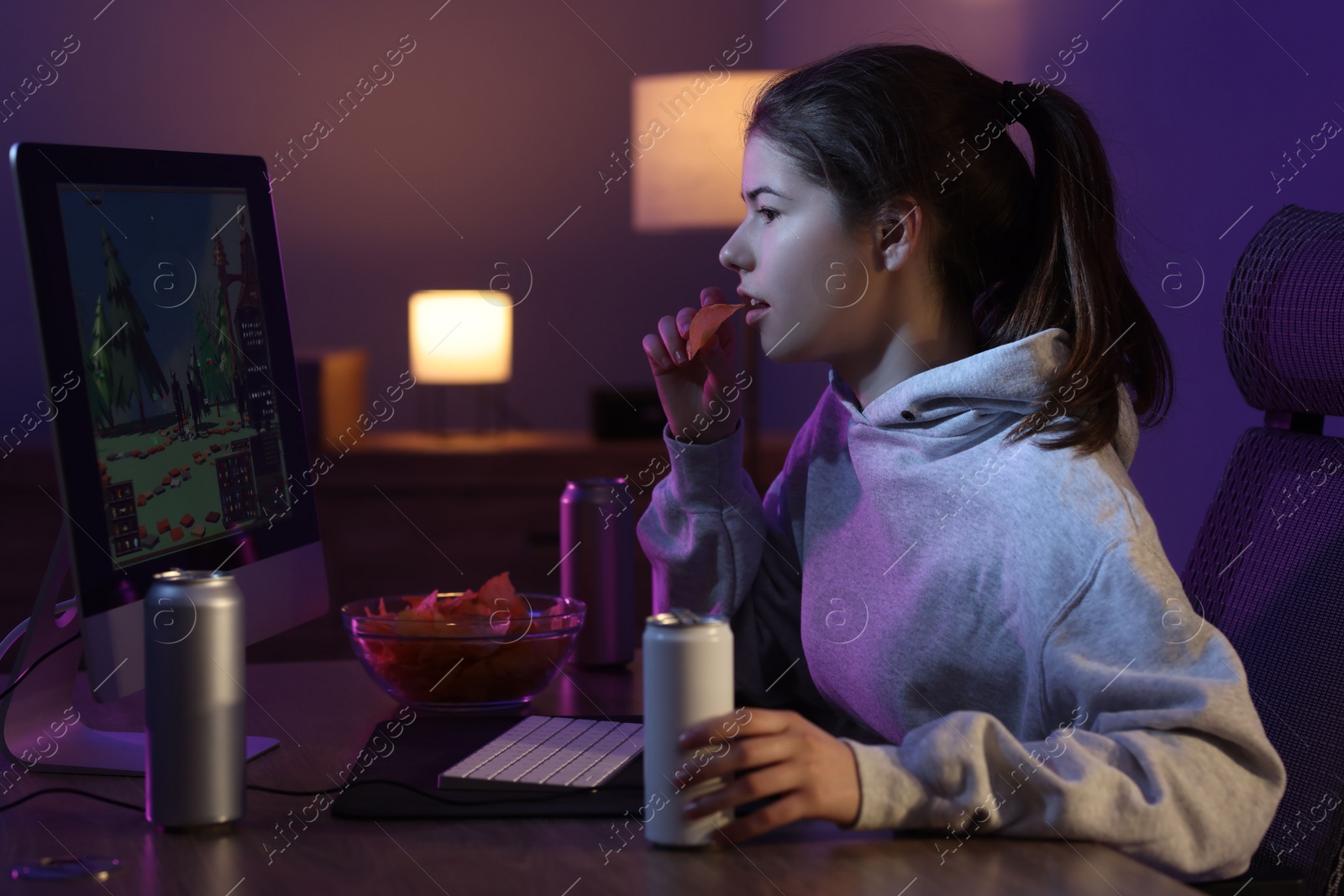 Photo of Girl with energy drink eating chips and playing computer game at home