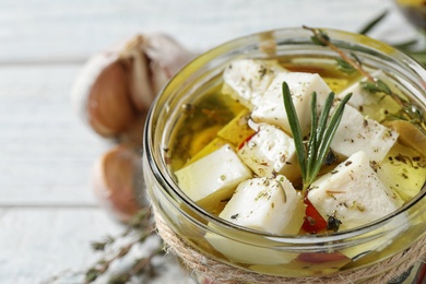 Pickled feta cheese in jar on white wooden table, closeup