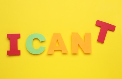 Photo of Motivation concept. Changing phrase from I Can't into I Can by removing paper letter T on yellow background, top view