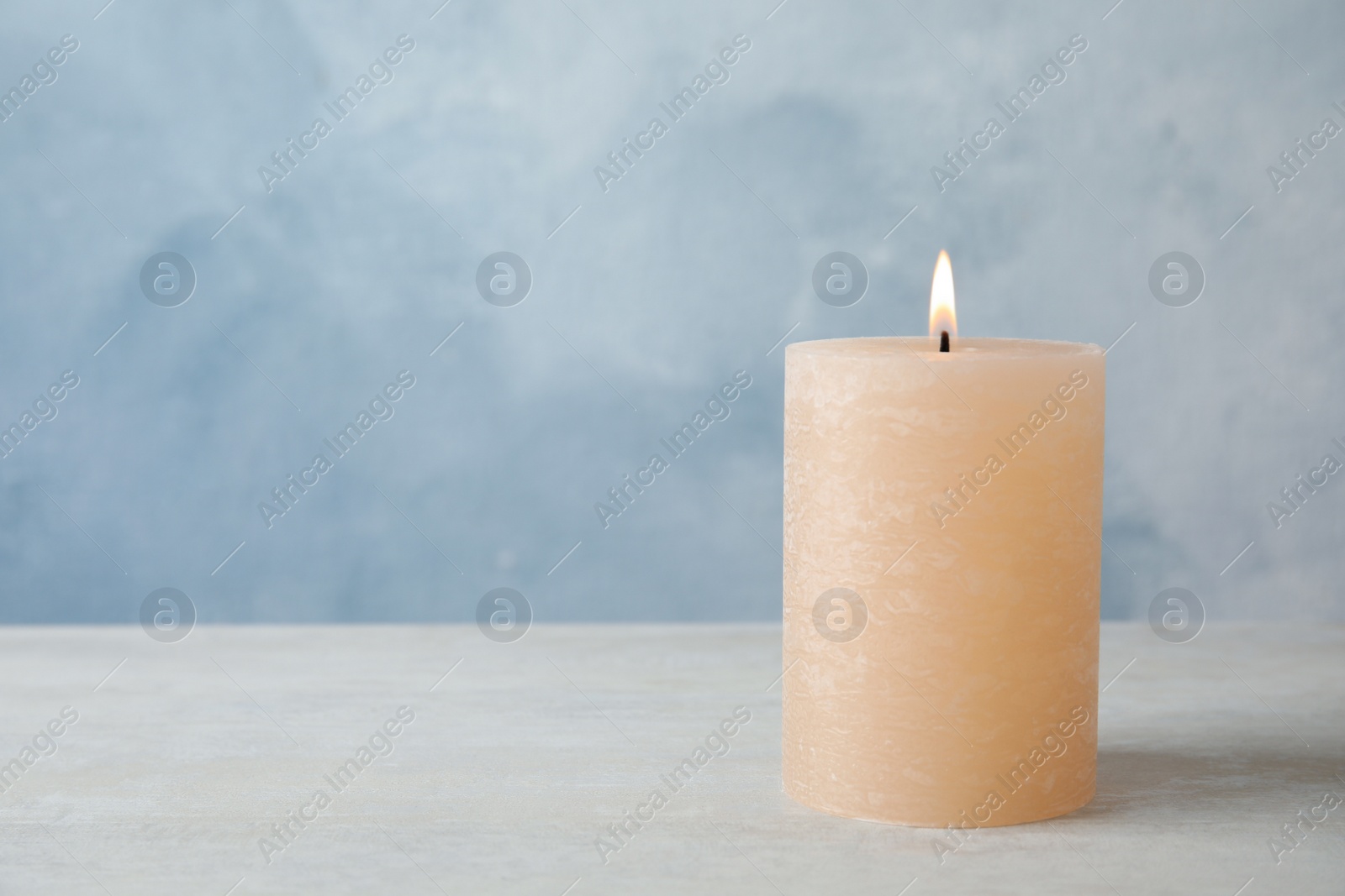 Photo of Burning candle on table against color background. Space for text