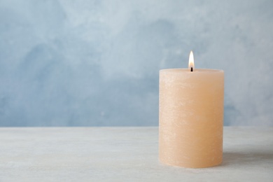 Burning candle on table against color background. Space for text