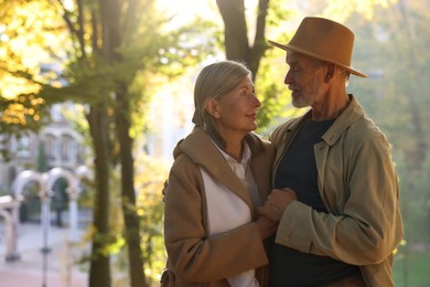 Affectionate senior couple in autumn park, space for text