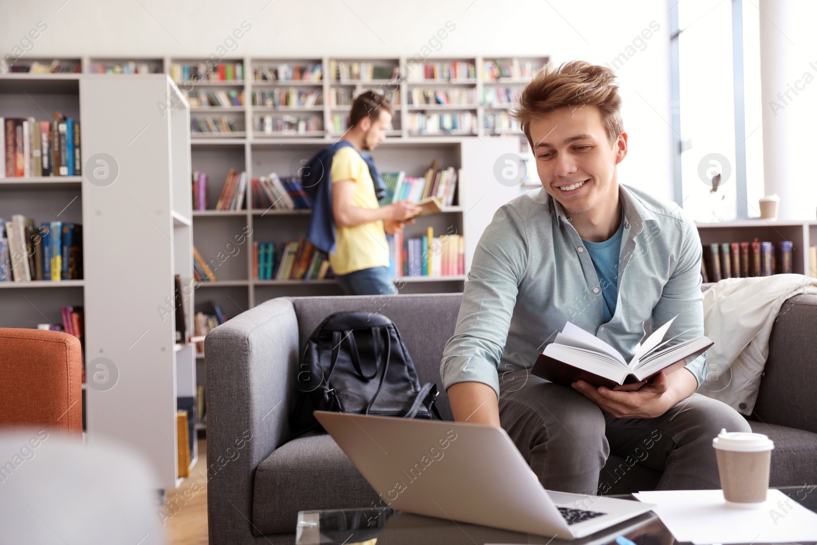 Photo of Young man studying on sofa in modern library