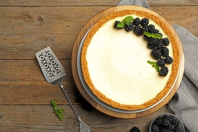 Photo of Delicious cheesecake decorated with blackberries on wooden table, flat lay