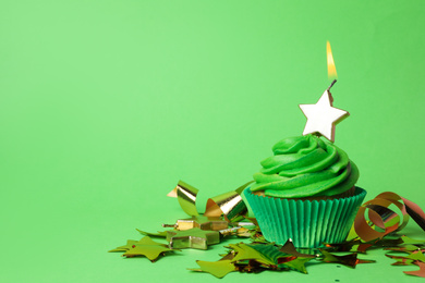 Delicious birthday cupcake with burning candle on green background. Space for text