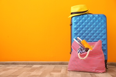 Photo of Suitcase and bag packed for summer journey on floor near color wall