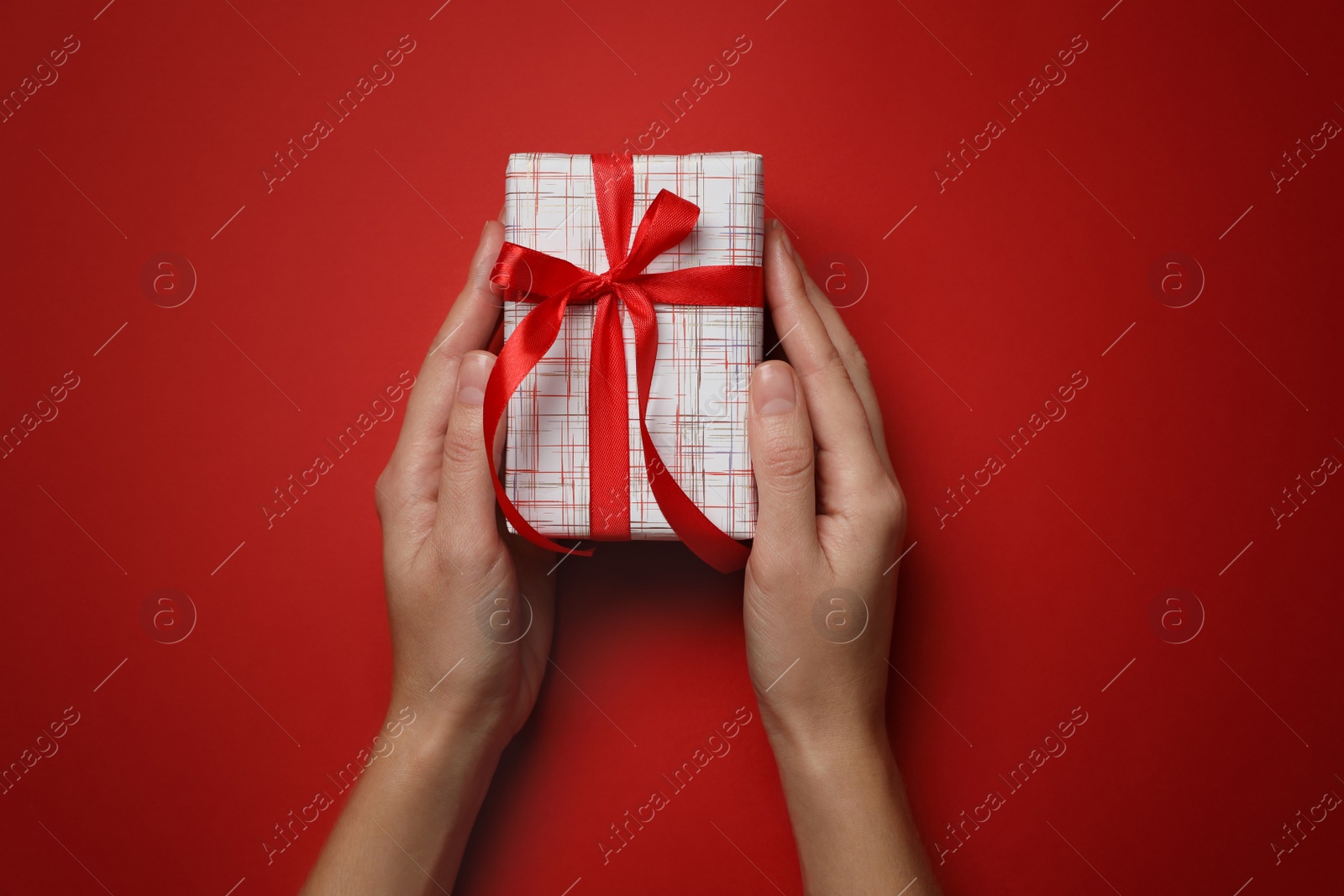 Photo of Woman holding Christmas gift on red background, top view