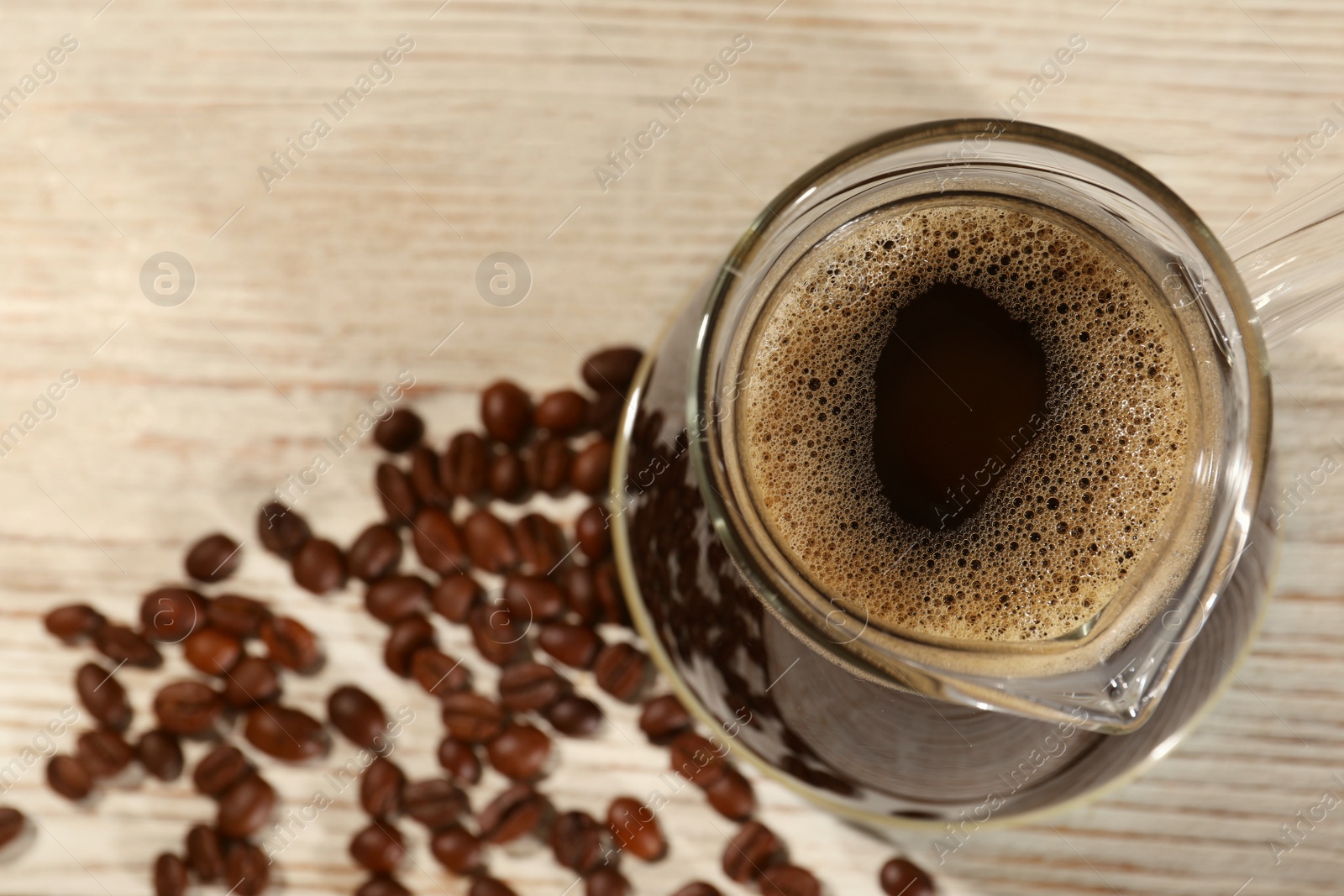 Photo of Glass turkish coffee pot with hot drink and beans on wooden table, top view. Space for text