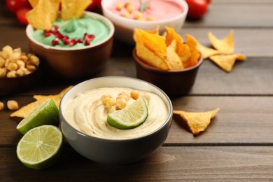 Photo of Different kinds of tasty hummus with ingredients on wooden table