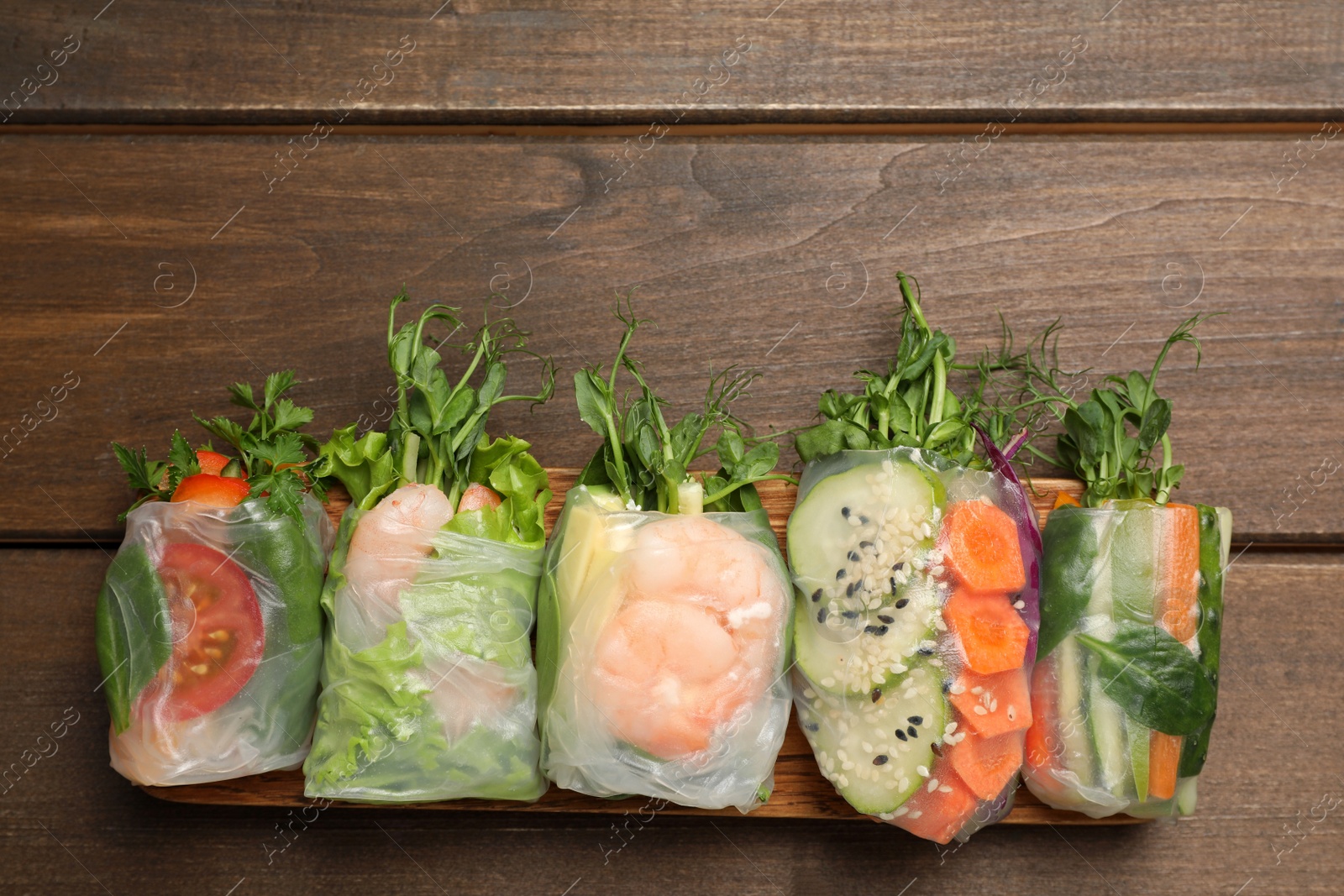 Photo of Many different delicious rolls wrapped in rice paper on wooden table, flat lay. Space for text