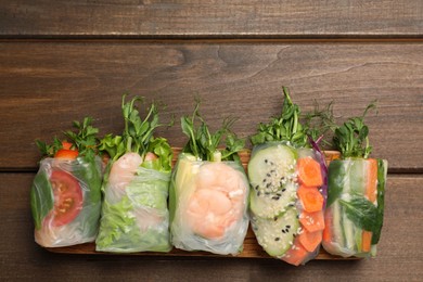 Many different delicious rolls wrapped in rice paper on wooden table, flat lay. Space for text