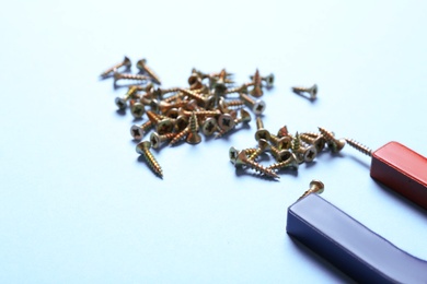 Photo of Magnet attracting screws on light blue background, closeup