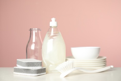 Photo of Cleaning supplies for dish washing and plates on white table against pink background