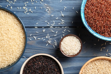 Flat lay composition with brown and other types of rice in bowls on color wooden background