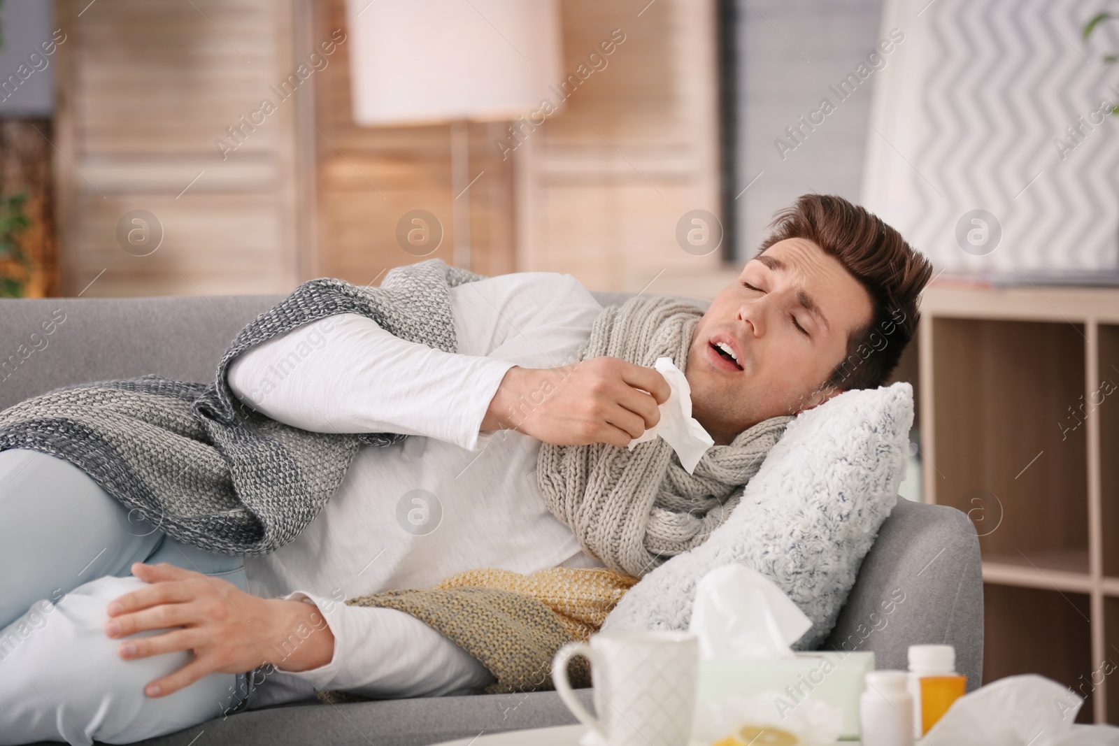 Photo of Sick young man with tissue suffering from cold on sofa at home