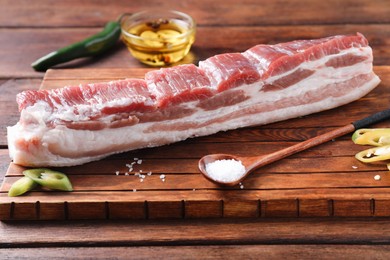 Photo of Piece of raw pork belly, green chili pepper, salt and oil with spices on wooden table, closeup