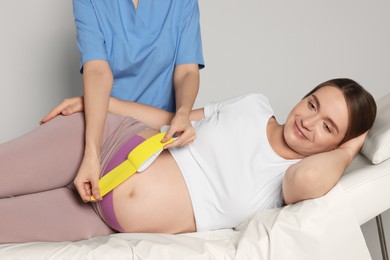 Photo of Pregnant woman visiting physiotherapist. Doctor applying kinesio tape indoors, closeup