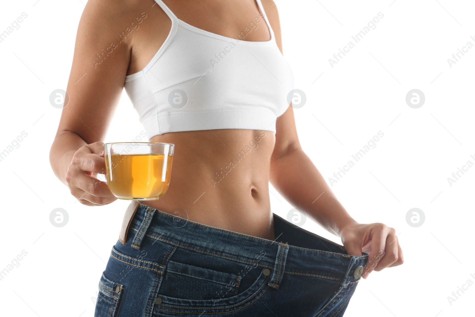 Photo of Young woman in old big jeans with cup of tea showing her diet results on white background, closeup