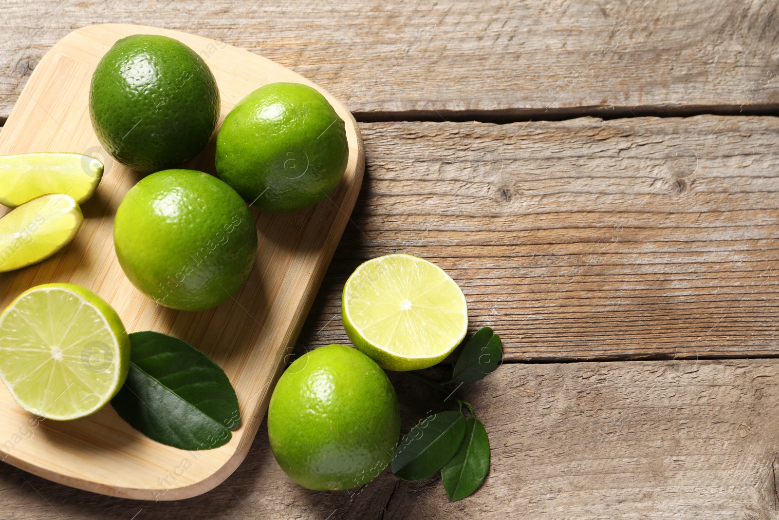 Photo of Fresh limes and green leaves on wooden table, flat lay. Space for text