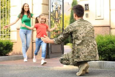 Photo of Happy family running to man in military uniform outdoors
