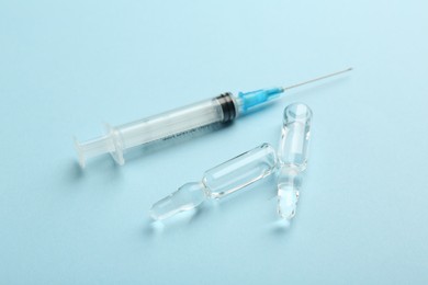 Glass ampoules with liquid and syringe on light blue background