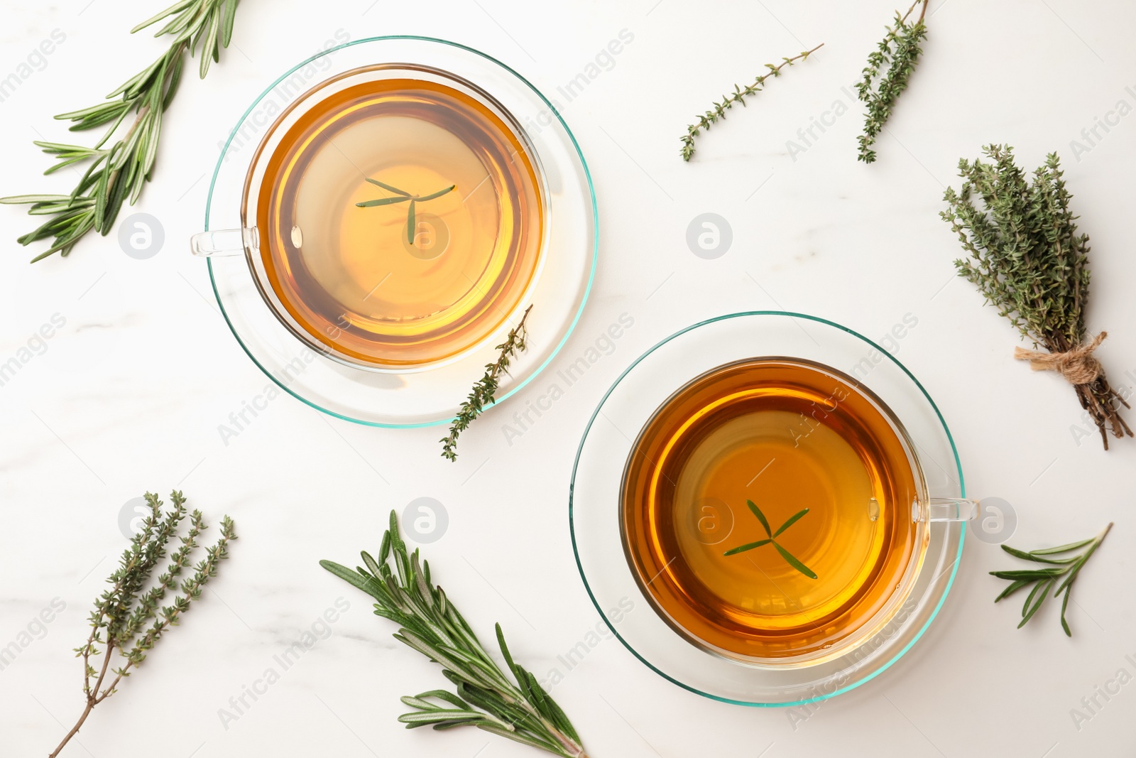 Photo of Cups of aromatic herbal tea with thyme and rosemary on white marble table, flat lay