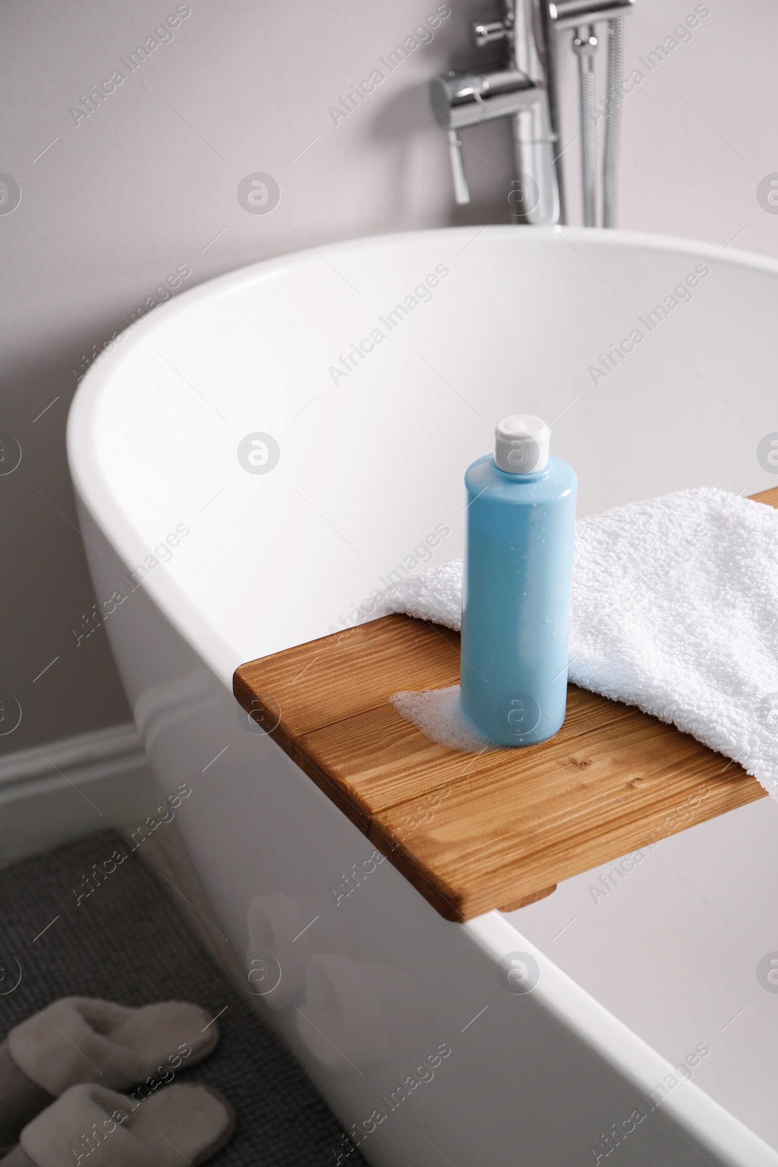 Photo of Bottle of bubble bath with foam and towel on tub in bathroom