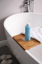 Bottle of bubble bath with foam and towel on tub in bathroom