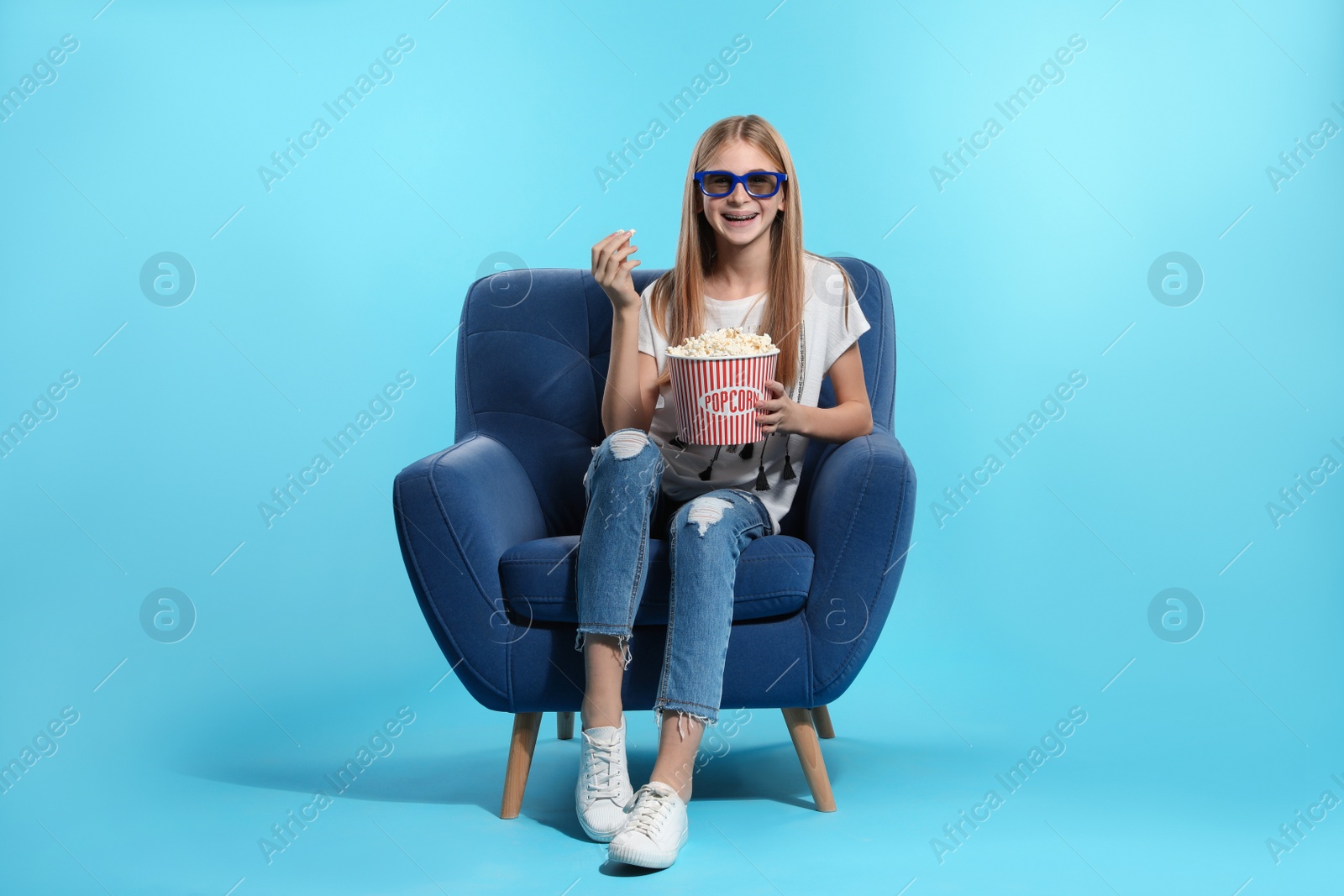 Photo of Teenage girl with 3D glasses and popcorn sitting in armchair during cinema show on color background