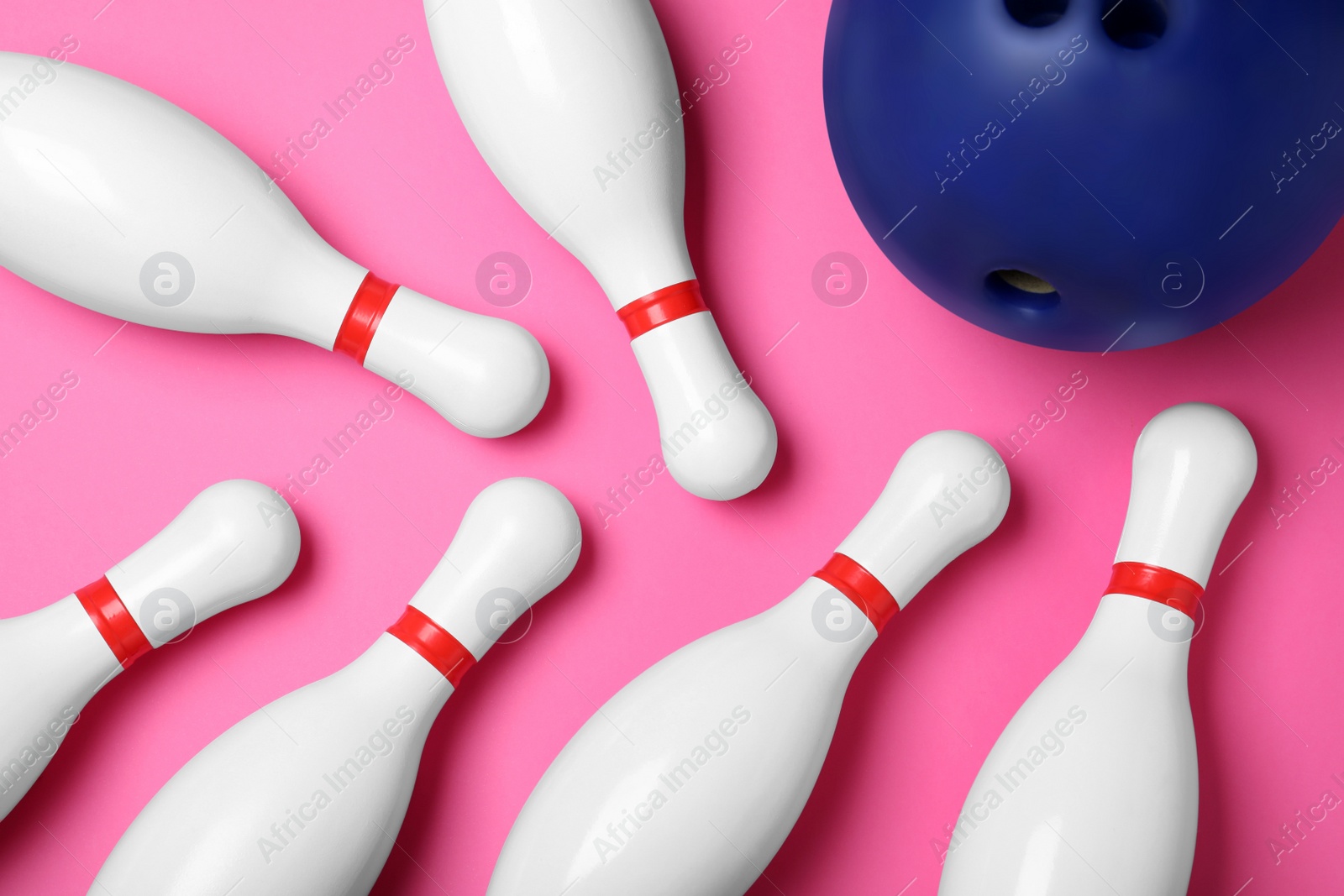 Photo of Bowling ball and pins on pink background, flat lay