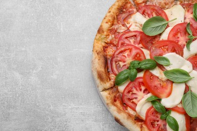 Photo of Delicious Caprese pizza with tomatoes, mozzarella and basil on light grey table, top view. Space for text