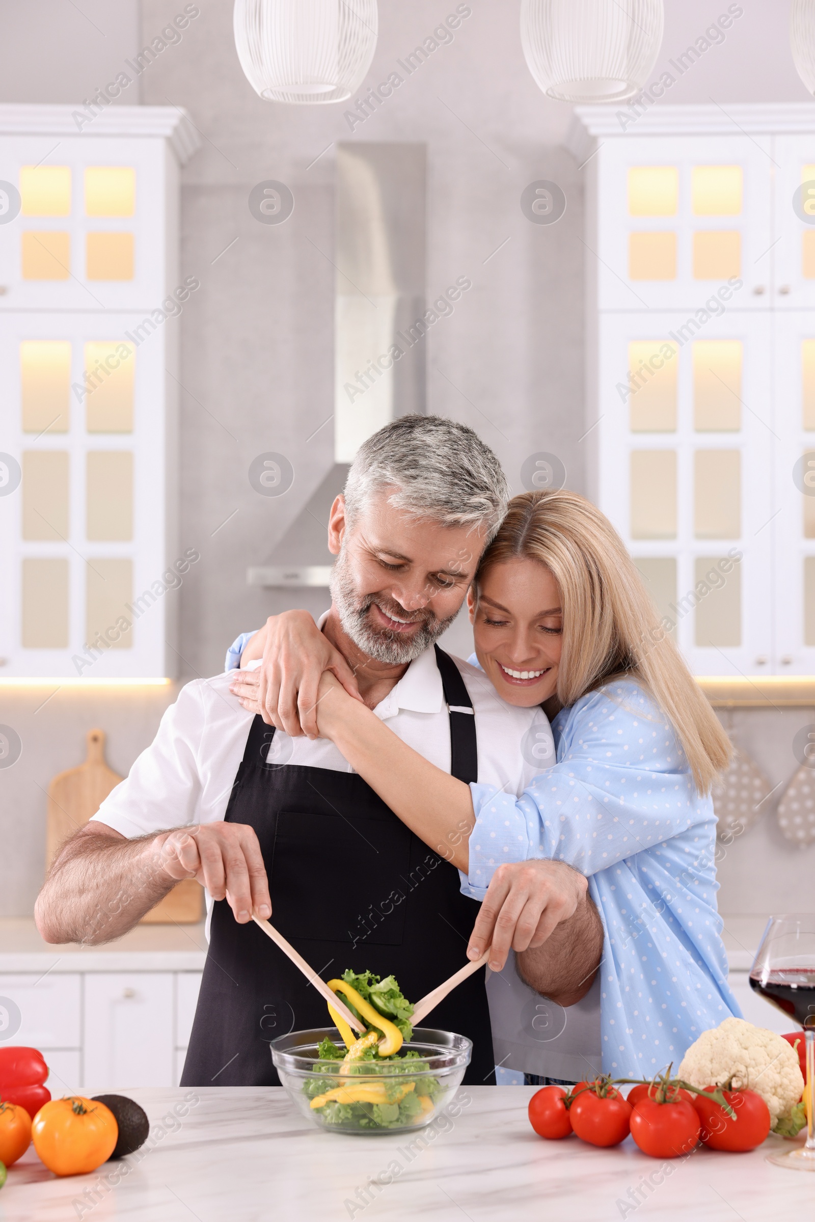 Photo of Happy affectionate couple cooking together at white table in kitchen