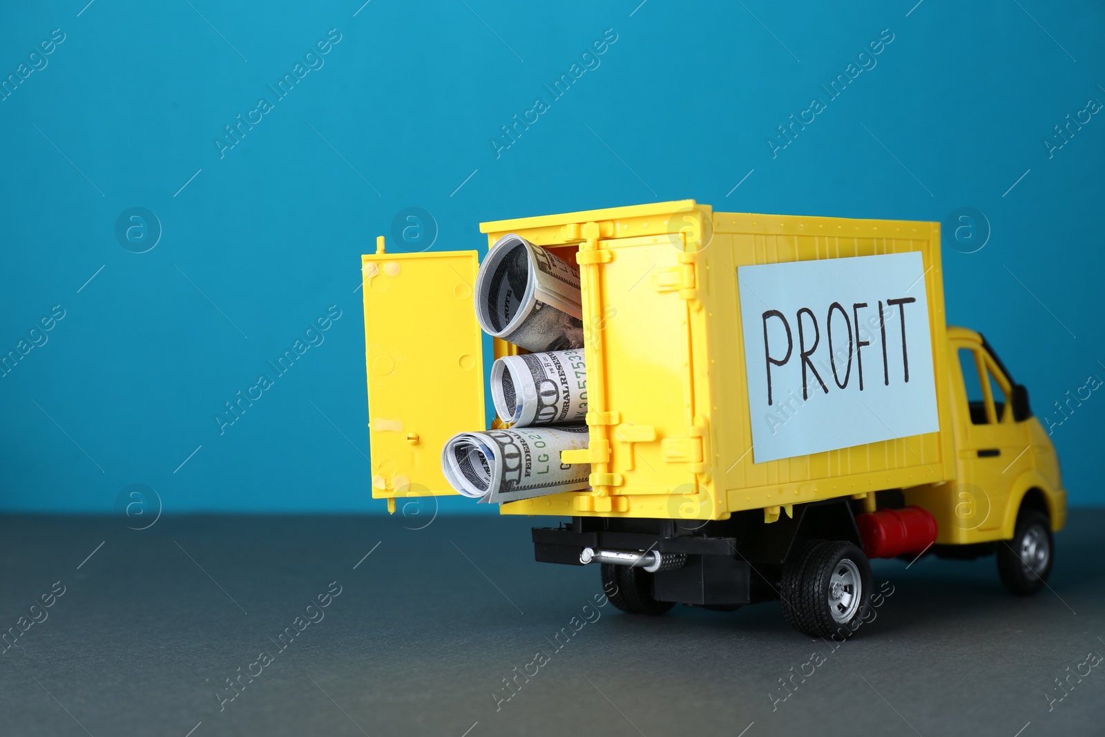 Photo of Economic profit. Toy truck with banknotes on grey table against light blue background, space for text