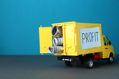 Photo of Economic profit. Toy truck with banknotes on grey table against light blue background, space for text