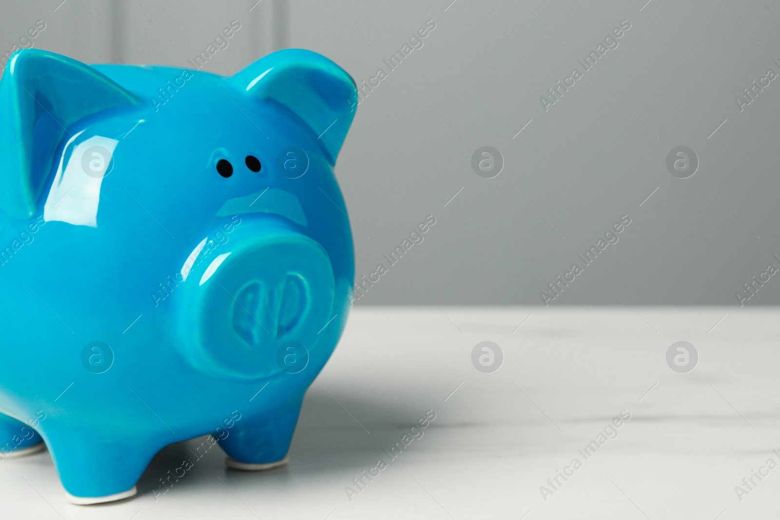Photo of Ceramic piggy bank on white marble table, closeup. Space for text