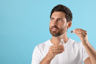 Handsome man with cosmetic serum on light blue background. Space for text