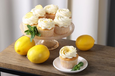Photo of Delicious lemon cupcakes with white cream, mint and lemons on wooden table