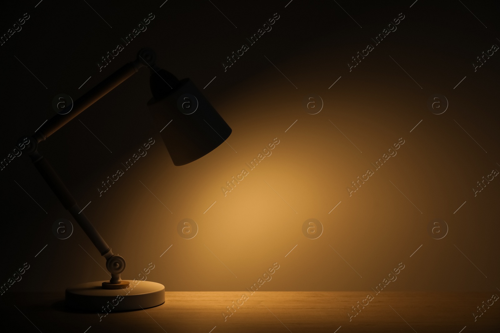 Photo of Stylish modern desk lamp on wooden table at night, space for text