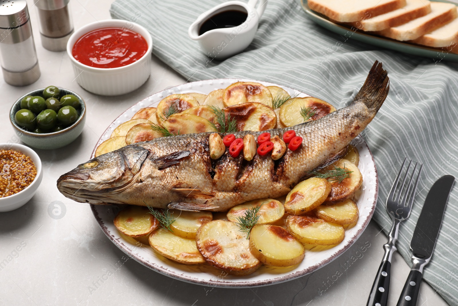 Photo of Plate with delicious baked sea bass fish and potatoes on table