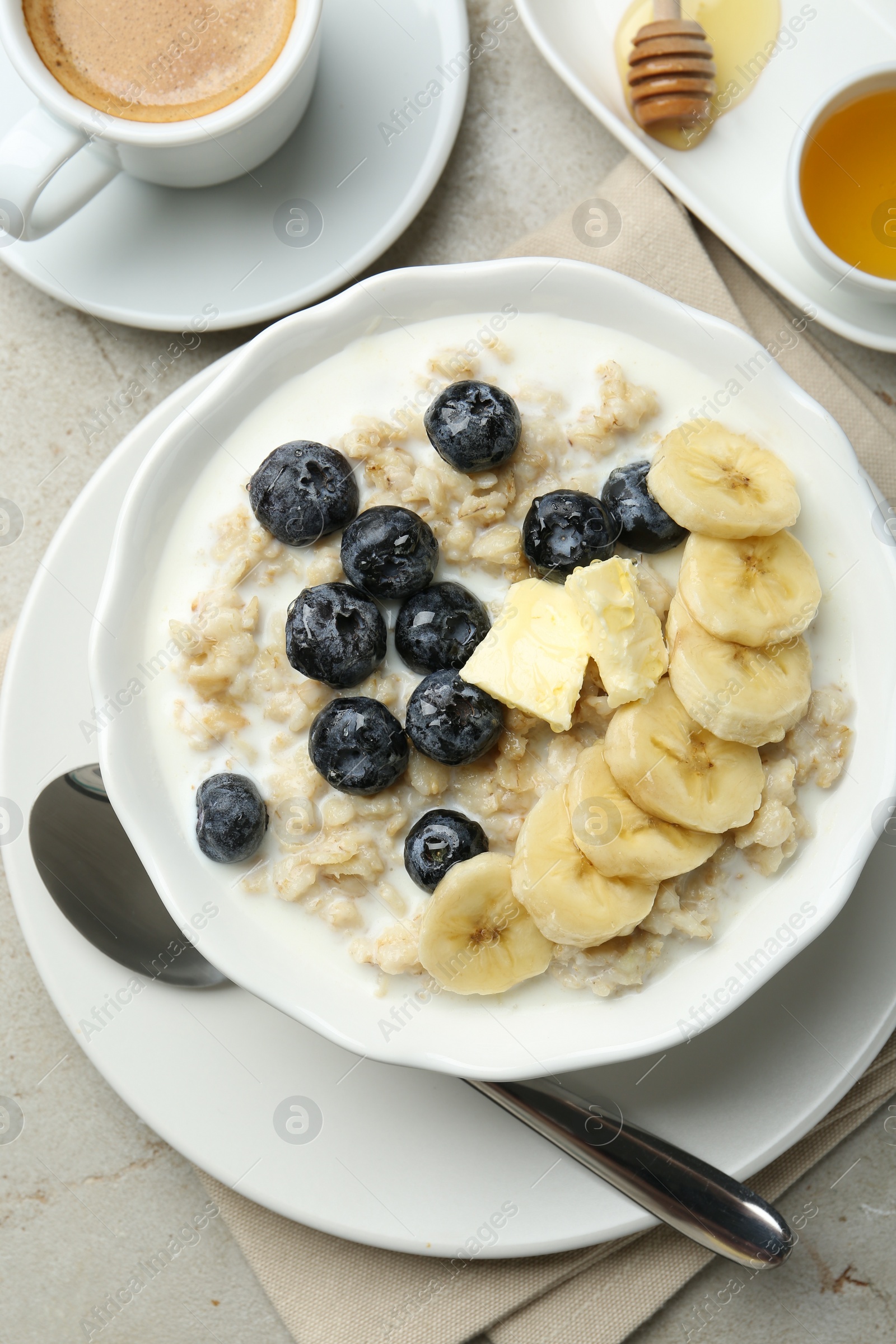 Photo of Tasty oatmeal with banana, blueberries, butter and milk served in bowl on light grey table, flat lay