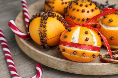 Photo of Pomander balls made of tangerines with cloves and candy canes on wooden table, closeup