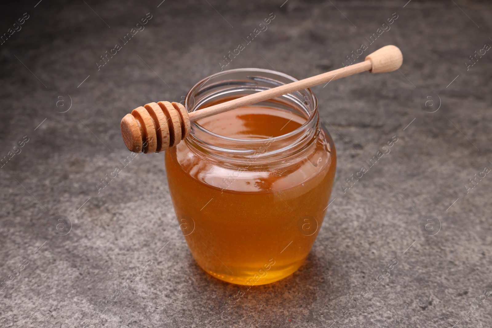 Photo of Sweet golden honey in jar and dipper on grey textured table