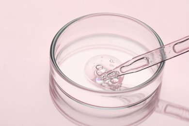 Photo of Glass pipette and petri dish with liquid on pink background, closeup