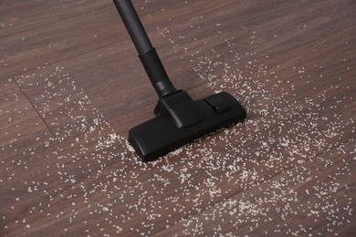 Vacuuming scattered rice from wooden floor in room