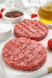 Photo of Raw hamburger patties with salt on board, closeup