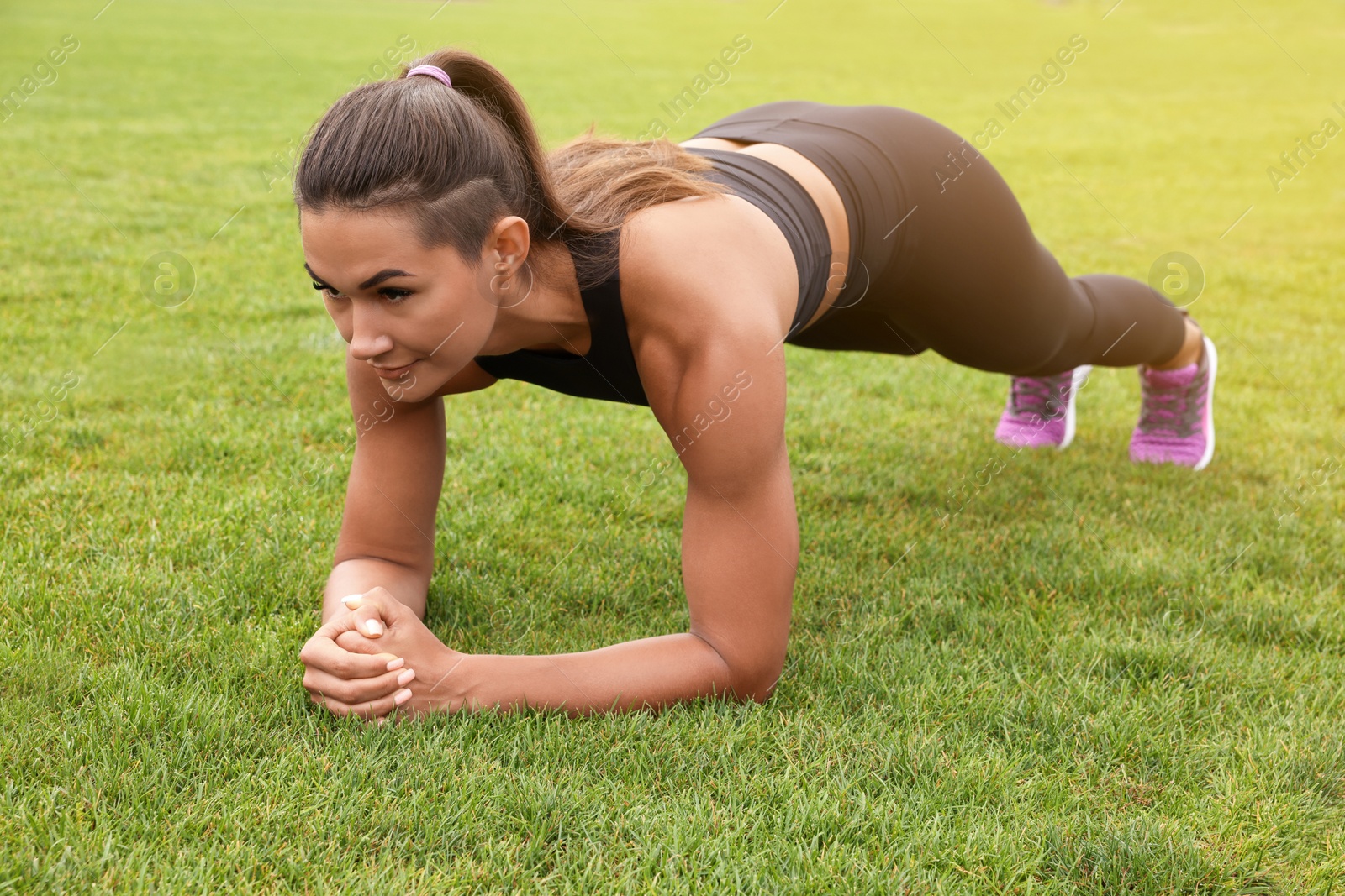 Photo of Young woman doing plank exercise on grass at stadium