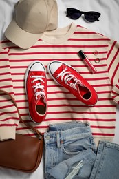 Pair of stylish red sneakers, clothes and accessories on white fabric, flat lay