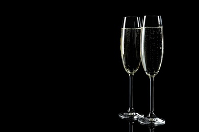 Photo of Glasses of champagne on black background, space for text