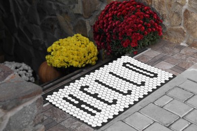 Stylish door mat with word HELLO and beautiful flowers on stairs