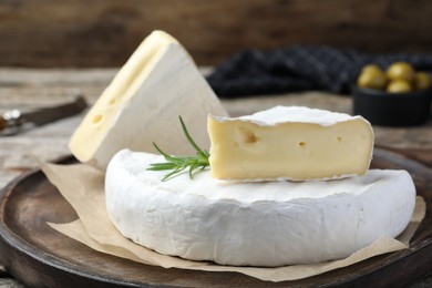 Tasty cut brie cheese with rosemary on wooden board